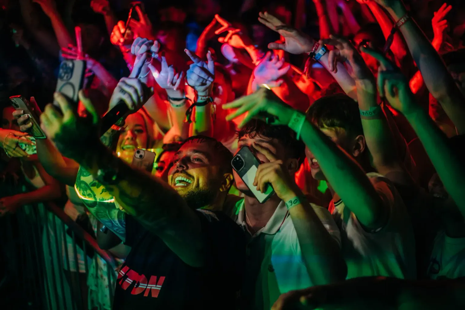Partygoers at the front of the crowd filming and dancing under coloured lights at Agenda White Party in Ayia Napa