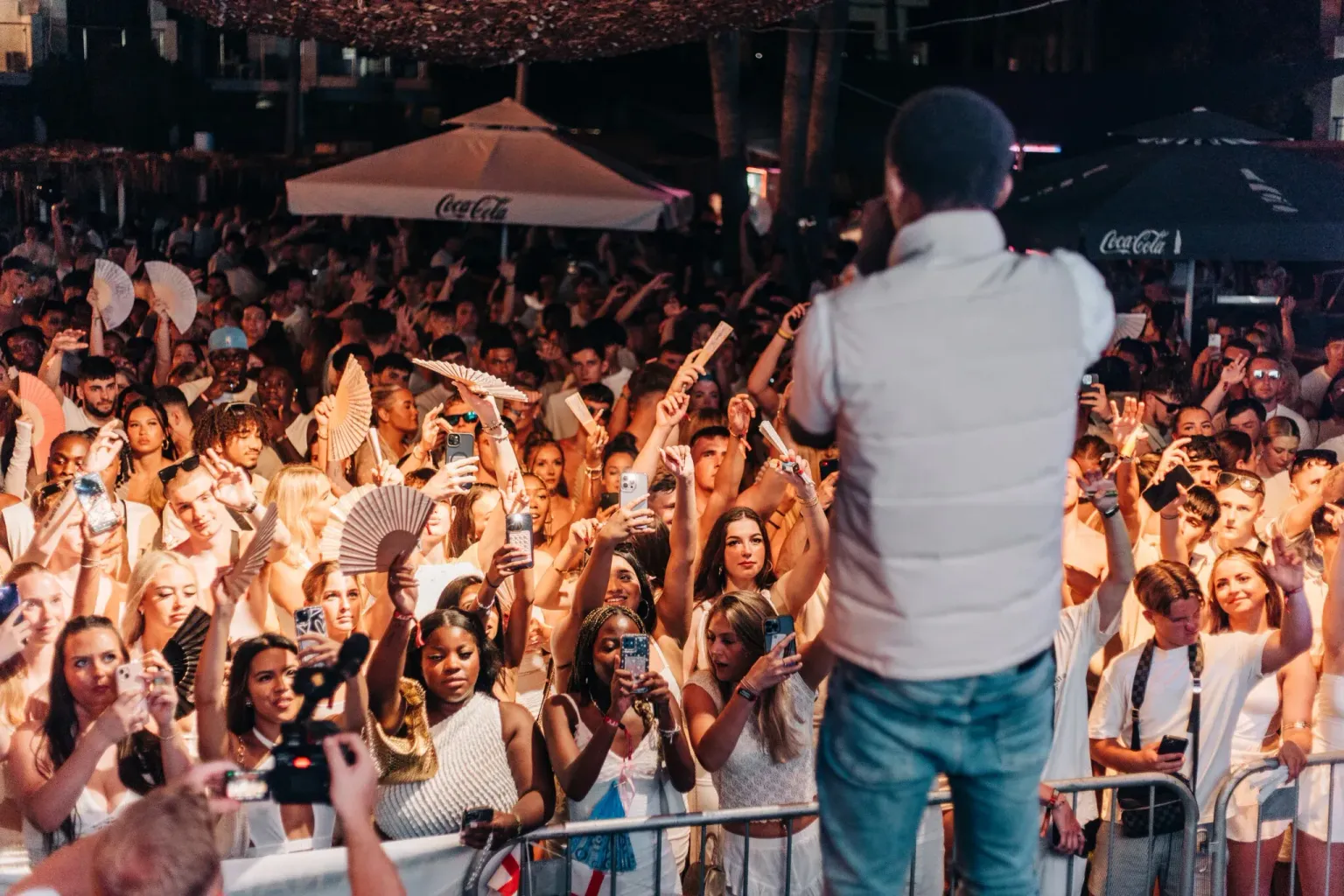 Live performer on stage facing a packed crowd dressed in white at the Agenda White Party in Ayia Napa at night