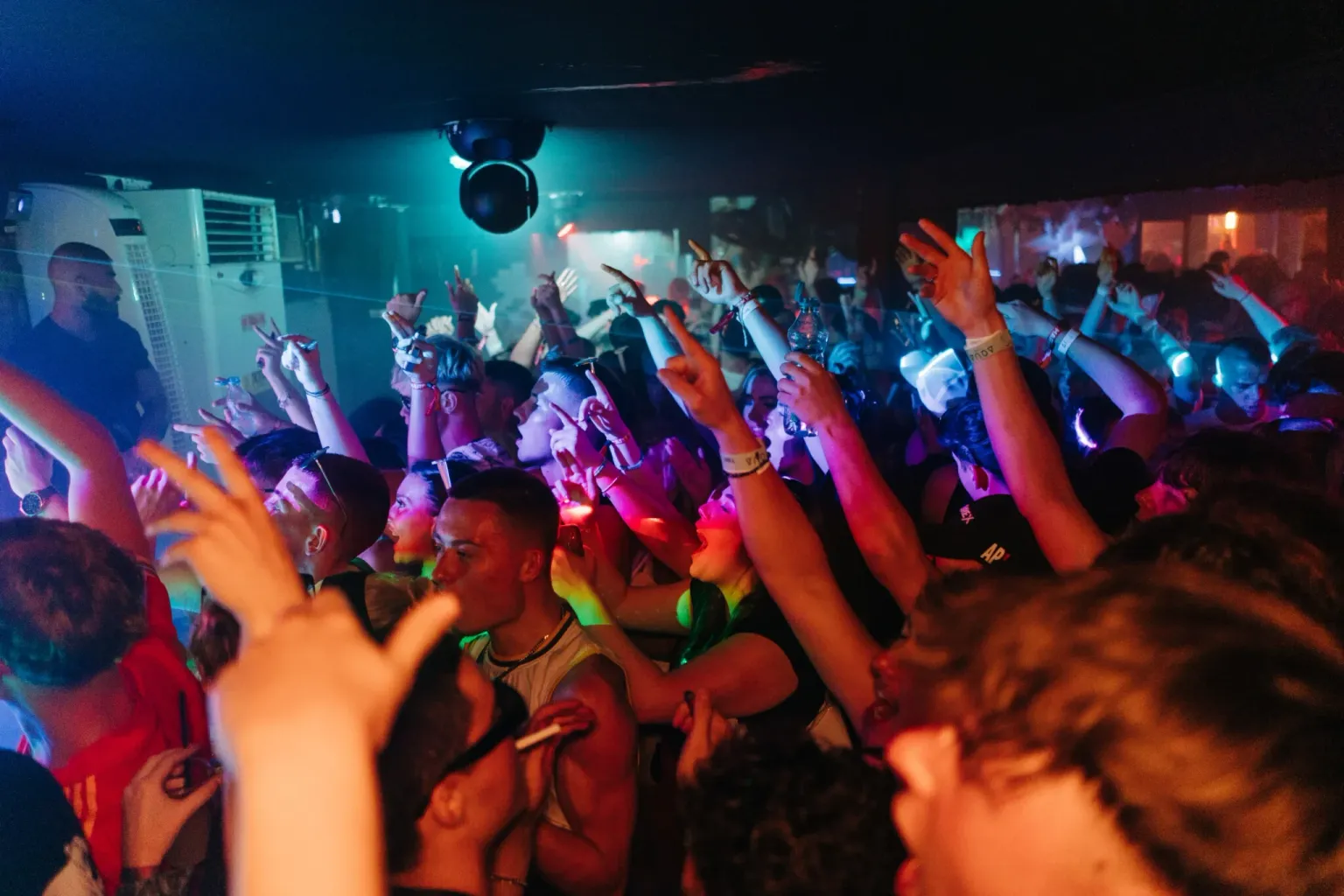 Club crowd dancing with hands raised under blue and red lighting at the House of Tech event in Ayia Napa