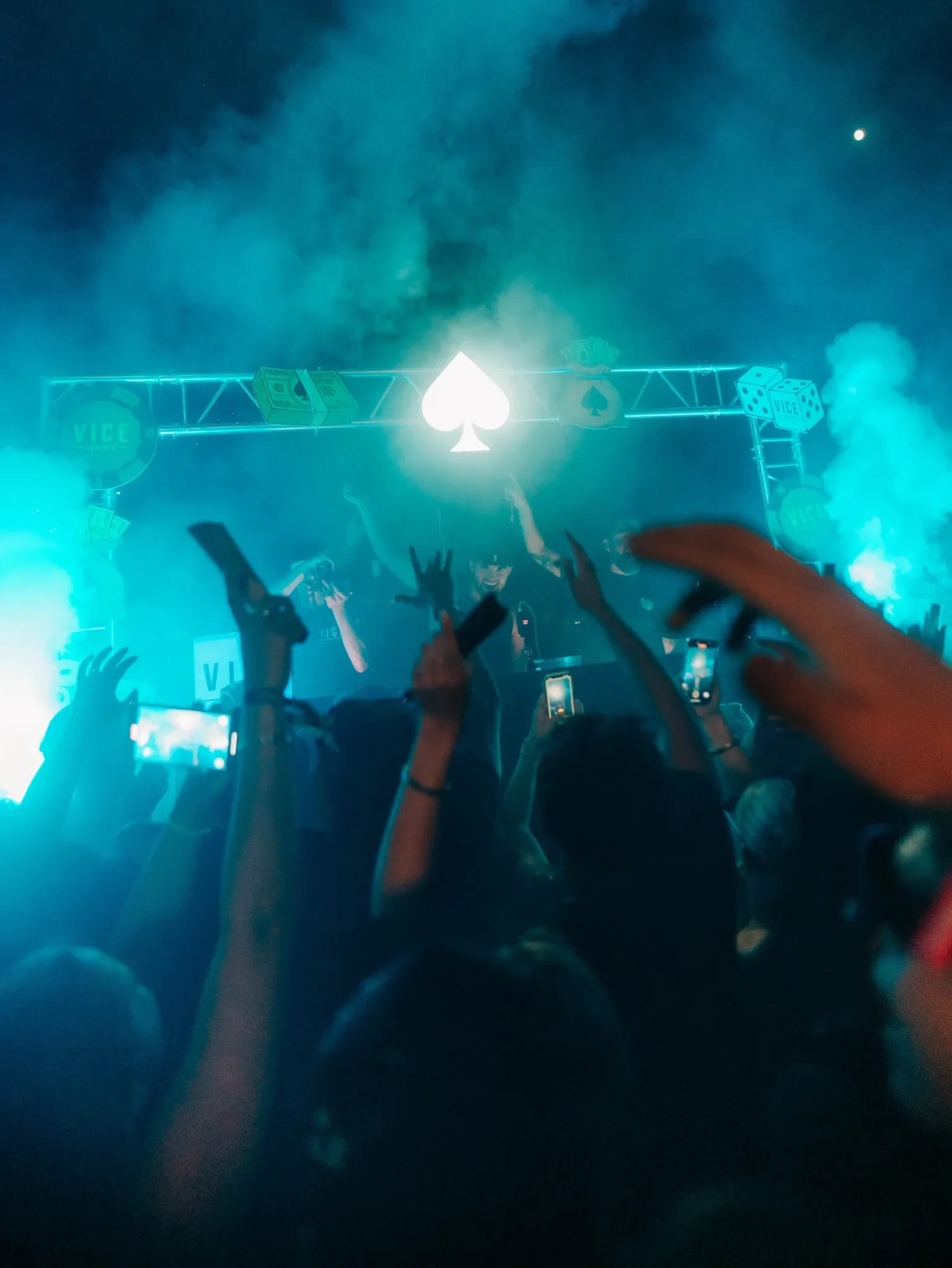 Crowd raising hands and filming as DJs perform under lights and smoke at the Vice Rooftop Party event in Ayia Napa.