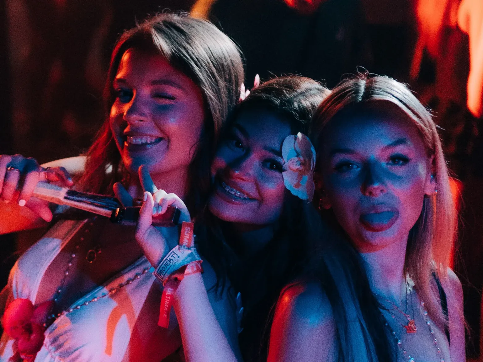 Three girls smiling and posing with playful expressions and flowers in their hair at the Lovejuice Residency event in Ayia Napa.