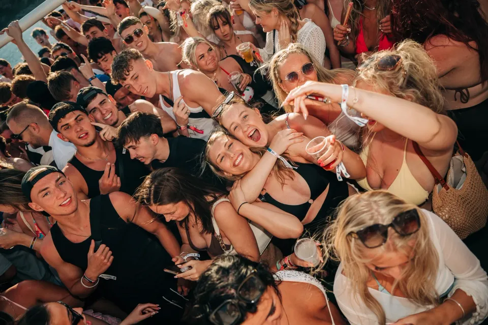 Lads and Girls mingling and laughing on the Malia Booze Cruise, drinks flowing and summer energy taking over the sun-soaked deck