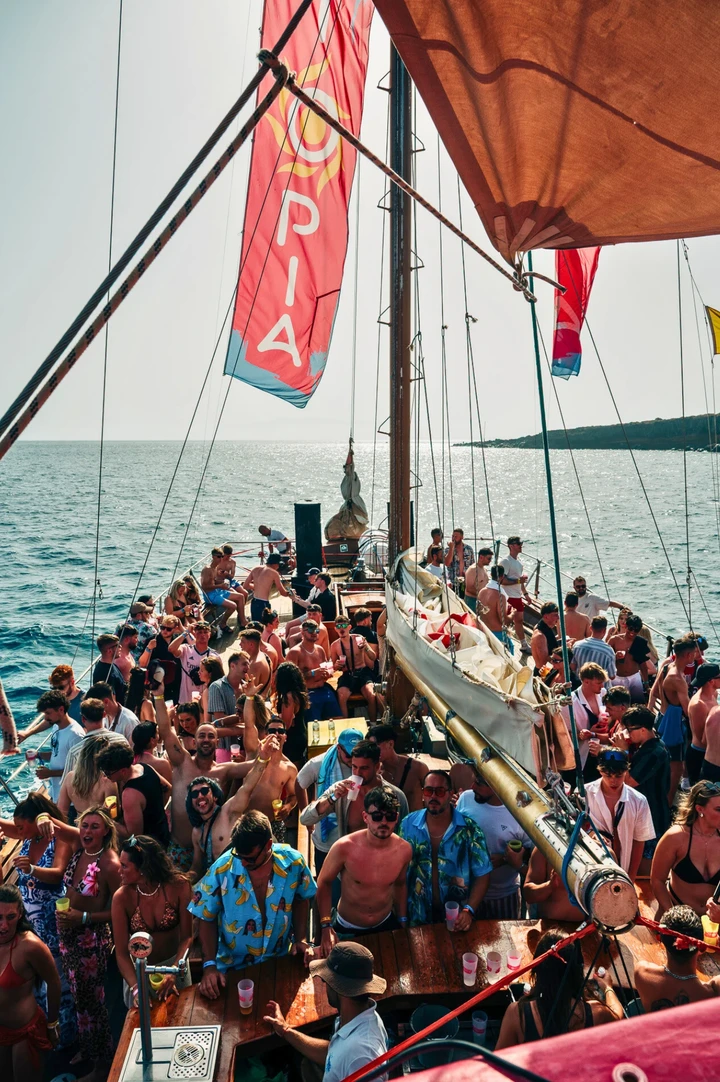 Packed Tenerife boat party with lads and girls dancing under UTOPIA flags, drinks up and full daytime chaos on deck