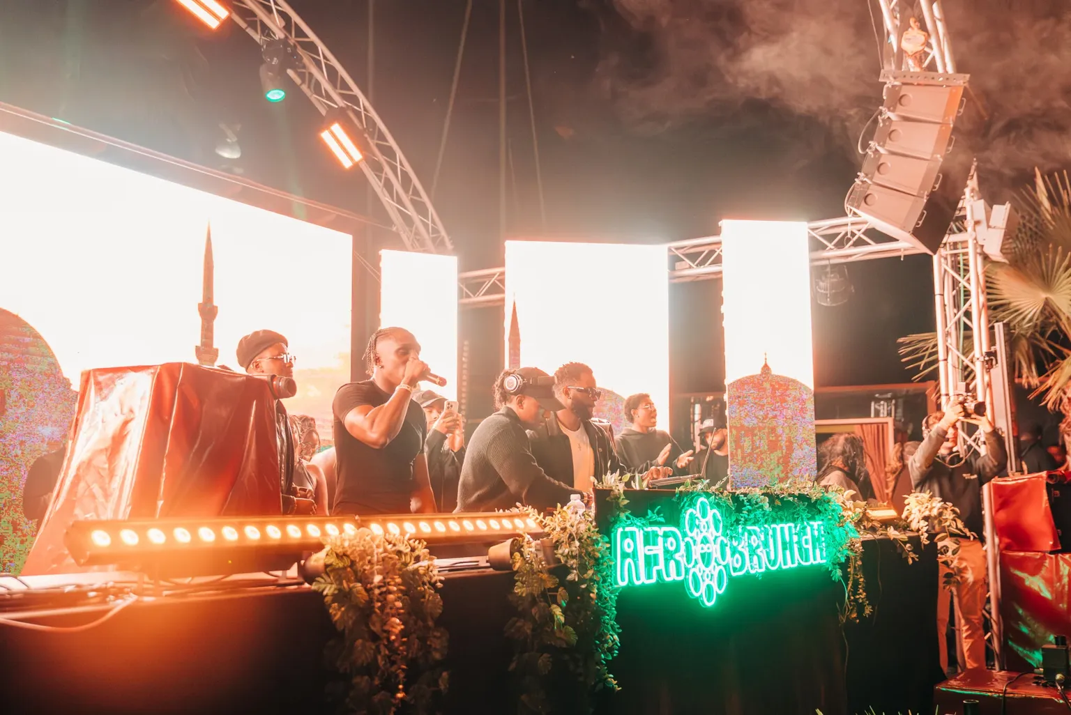 DJs and MCs powering a high-energy Barcelona set on a lit-up stage, hyping the venue with bright screens and intense atmosphere.