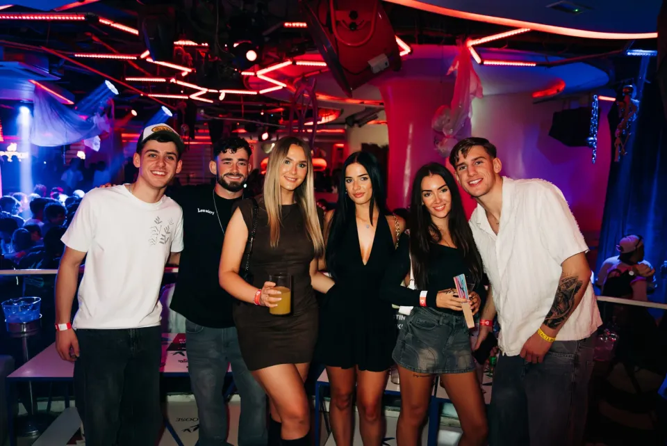 Group of lads and girls in a packed Barcelona nightclub with neon lights and drinks, ready for a big night out with Party Hard vibes.