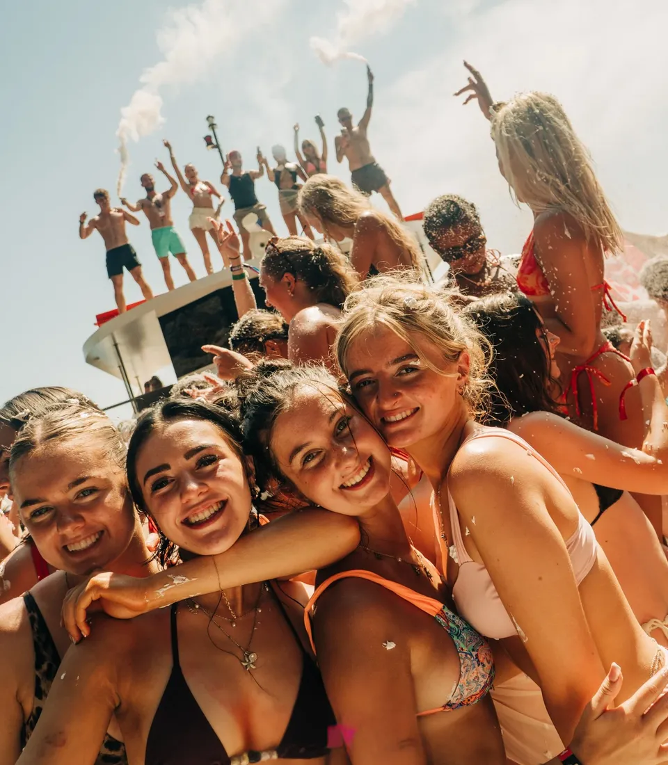 Girls posing together on a crowded Kavos boat party with people dancing and smoke flares behind them