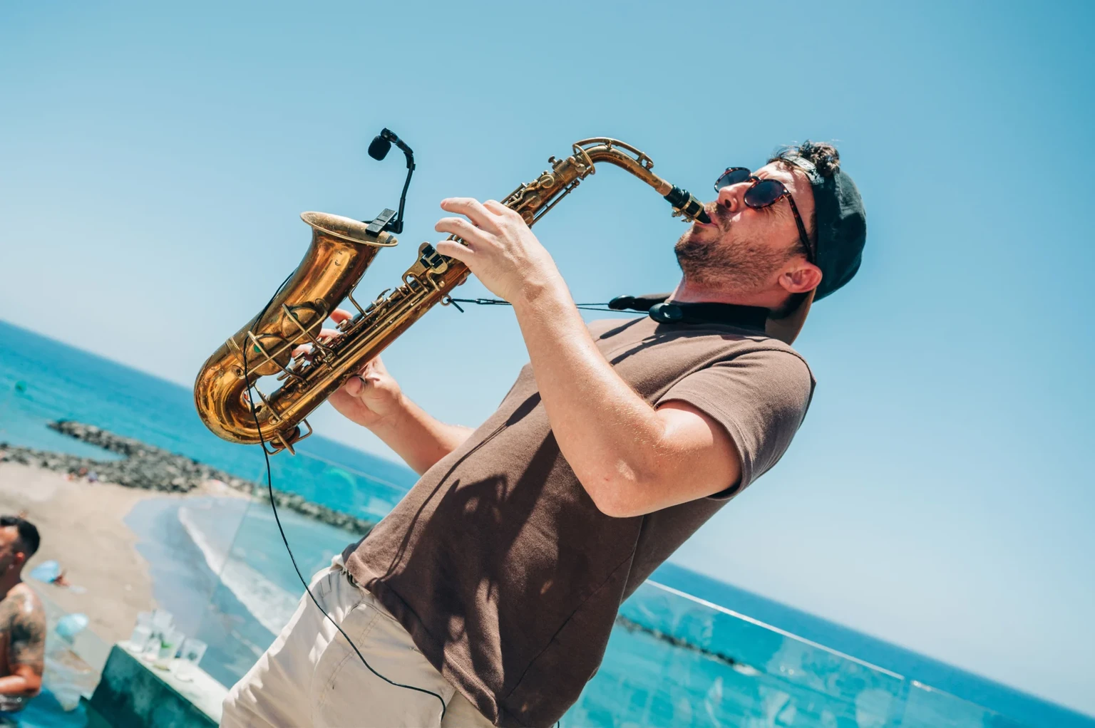 Sax player performing poolside at a Tenerife day party, shades on, ocean views and the crowd soaking up the vibes