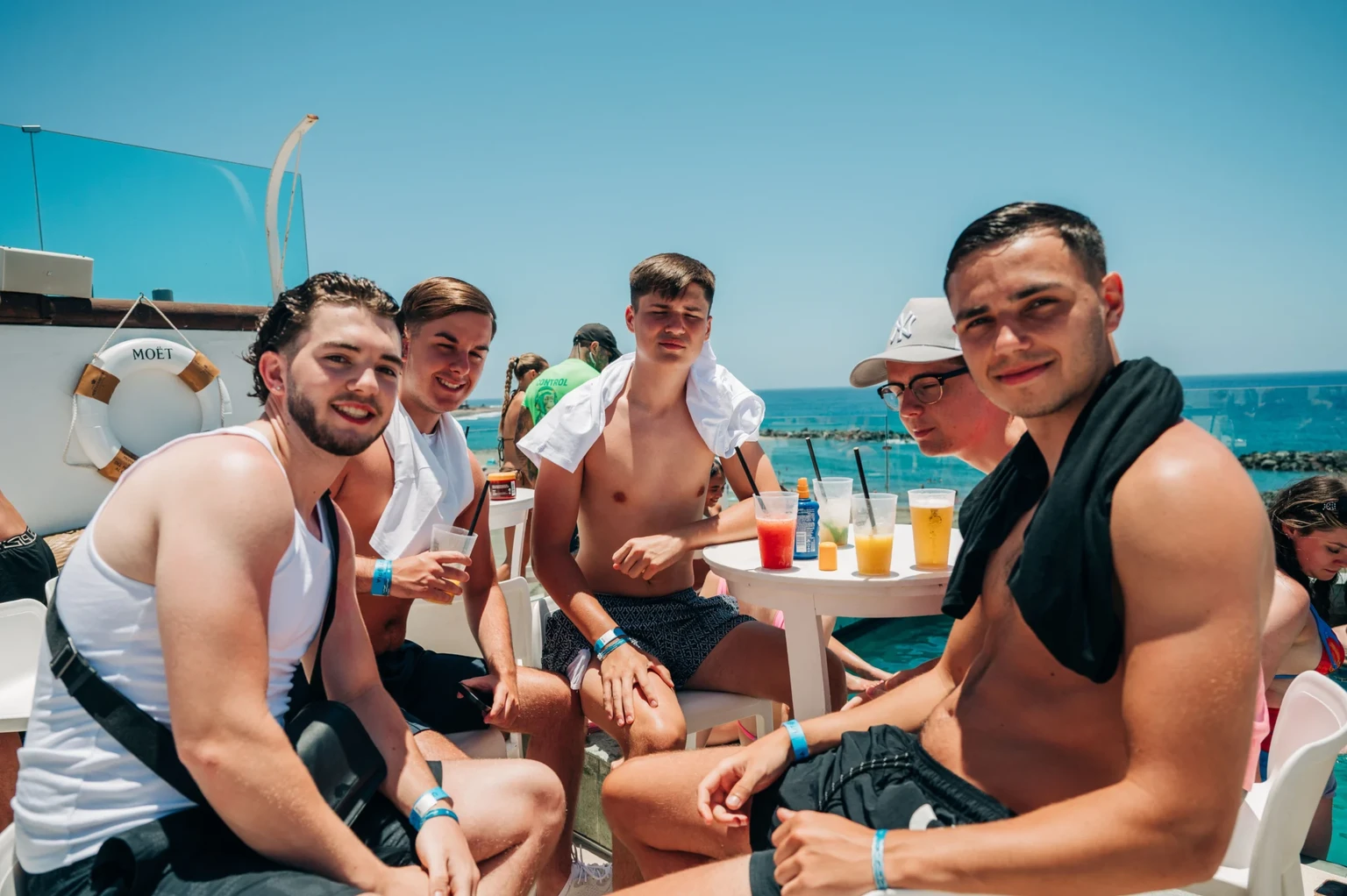 Group of lads chilling poolside in Tenerife, cold beers on the table, sun out, sea views and daytime party energy