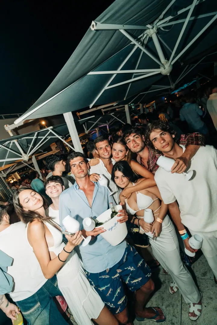 Big group raising glasses at Cafe Del Mar Malta, white outfits glowing under night lights and DJs keeping the terrace jumping