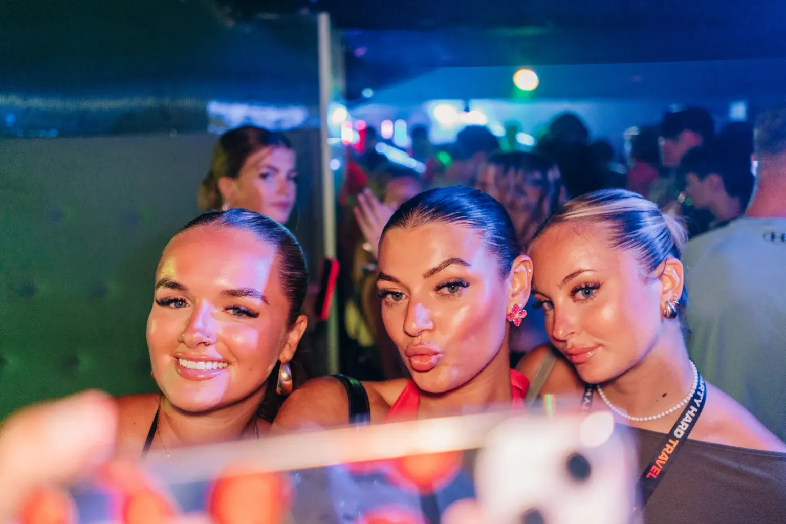Three girls posing together under colourful club lights during the LoveJuice Residency night in Ayia Napa