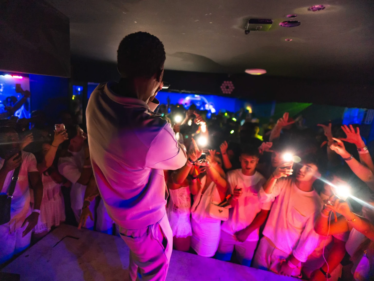 Performer on stage facing the crowd with phones raised at Napa Xtra event in Aqua Club Ayia Napa