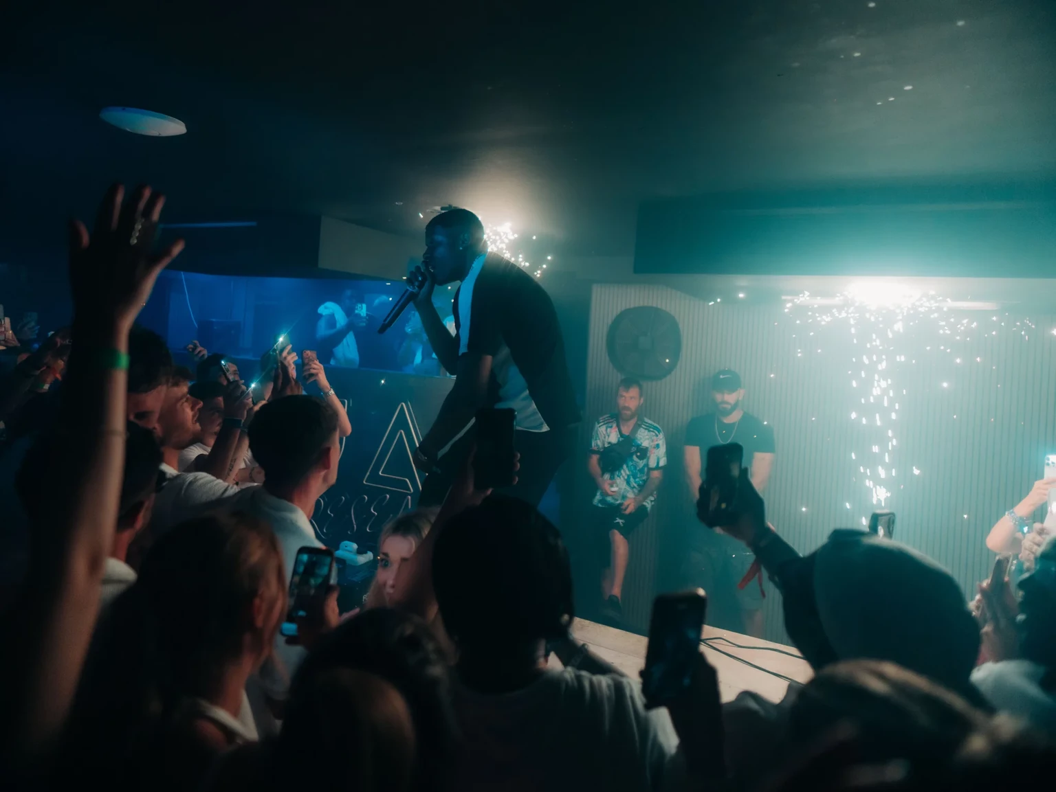 Napa Xtra artist on the mic above the front row at Aqua Club in Ayia Napa as phones glow and sparklers hit the room