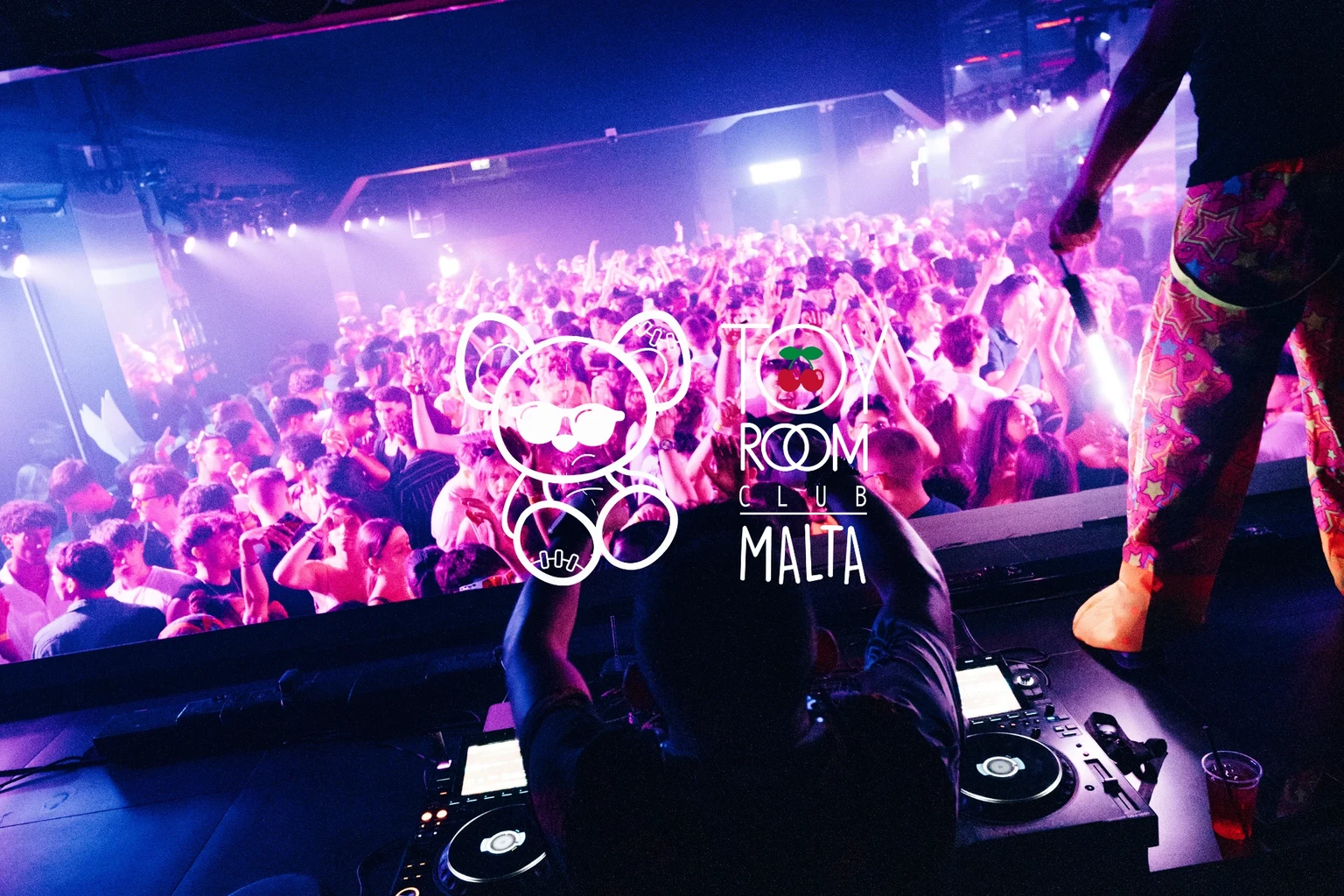 DJ booth view of Toy Room Super Club Night in Malta, with a packed crowd, purple club lights and the Toy Room logo over the image.
