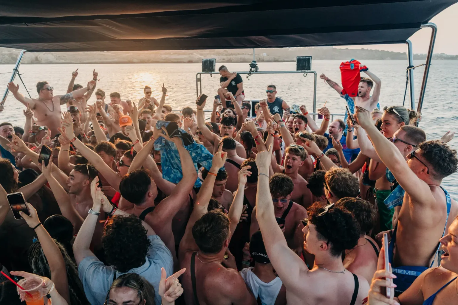 Crowd dancing with hands raised on the Fantasy Boat Party off the coast of Ayia Napa during a summer sunset