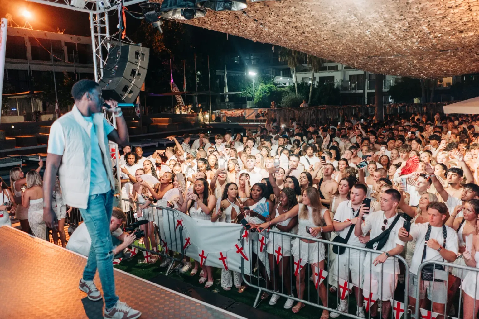 Live performer Hardy Caprio on stage facing a packed crowd dressed in white at the Agenda White Party in Ayia Napa at night