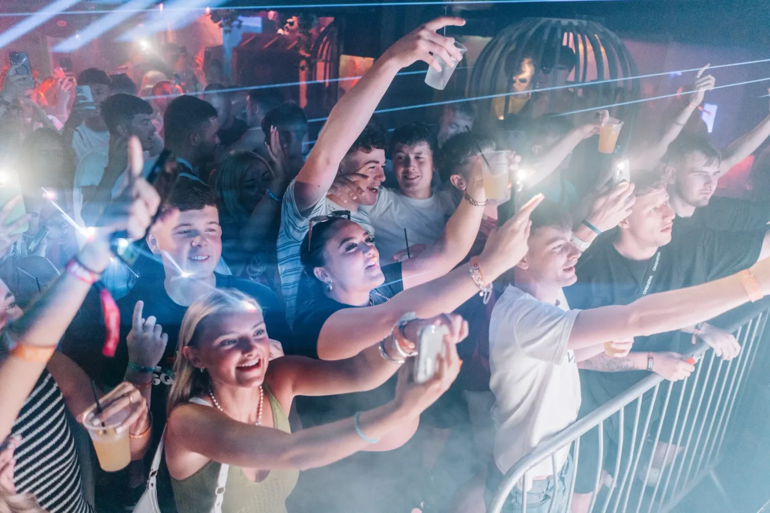 Partygoers dancing under colourful club lights with phones raised at the House of Tech event in Ayia Napa